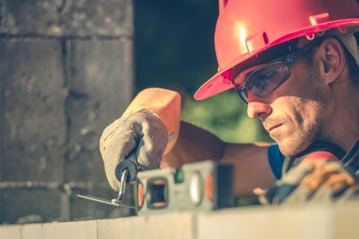 Worker in red hard hat measuring metal with a tape measure at a construction site