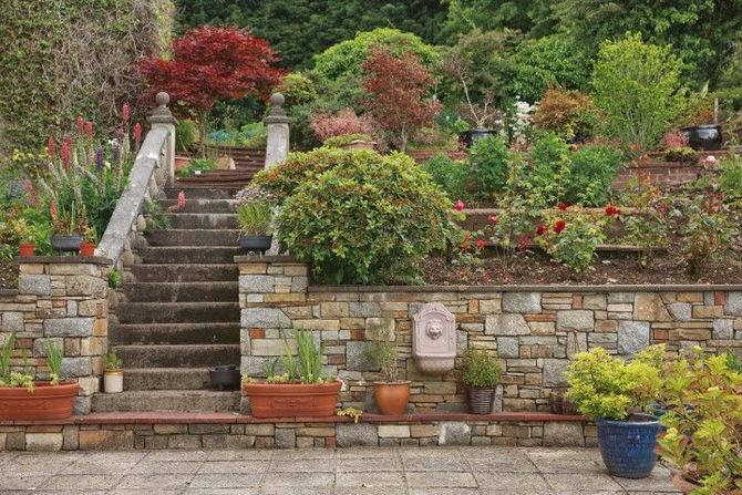 Stone garden terrace with stairs, potted flowers, and lush greenery on a landscaped hillside