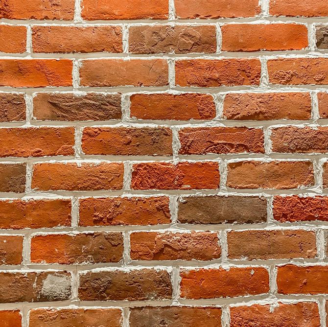 Red brick wall with white mortar and scattered weathered, uneven bricks.