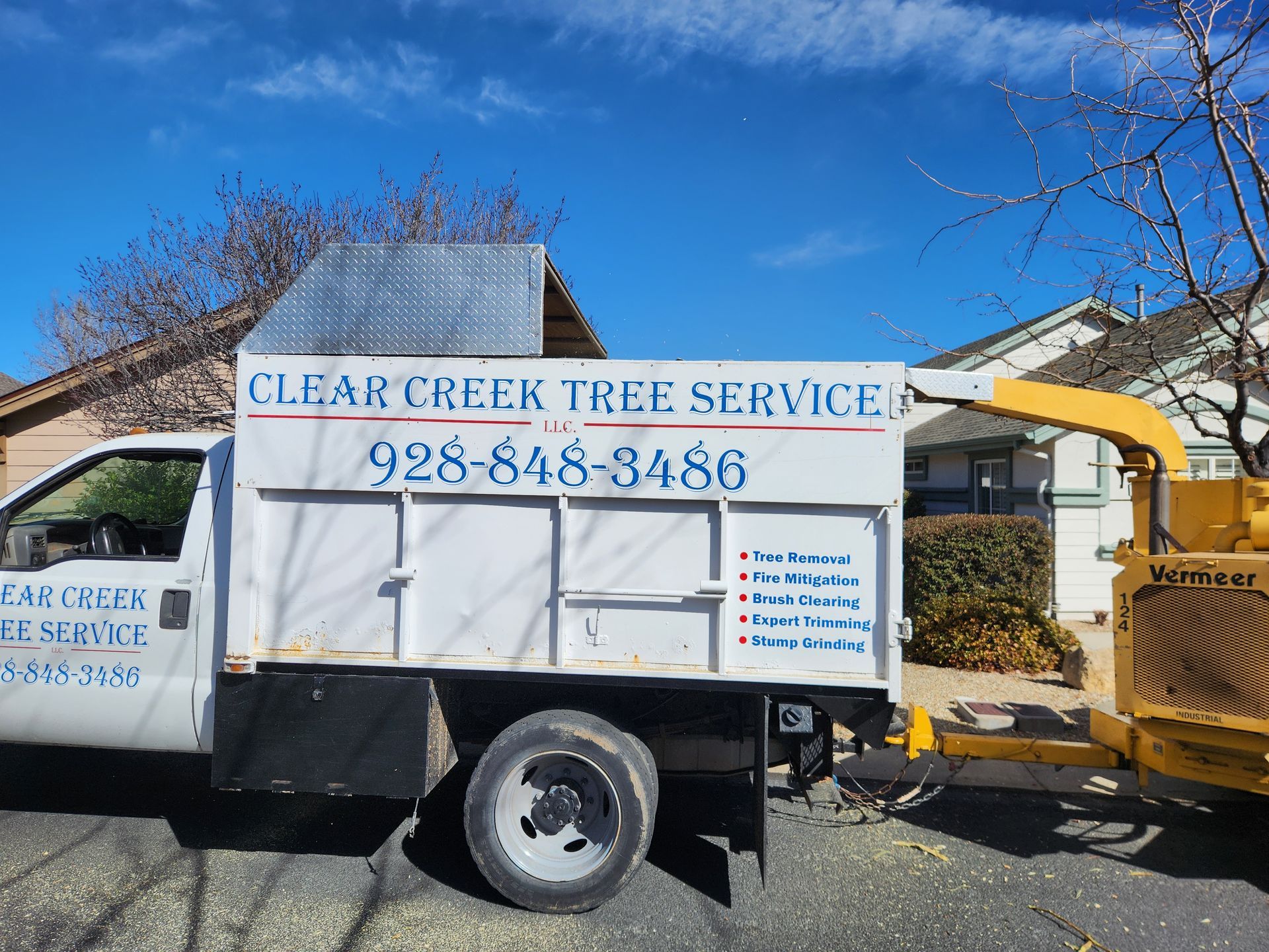 A white Clear Creek Tree Service truck with phone number 928-848-8486 and chipper against a blue sky.