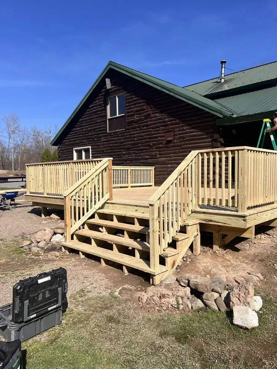 A new, light-colored wooden deck with stairs attached to the side of a dark brown cabin-style house.