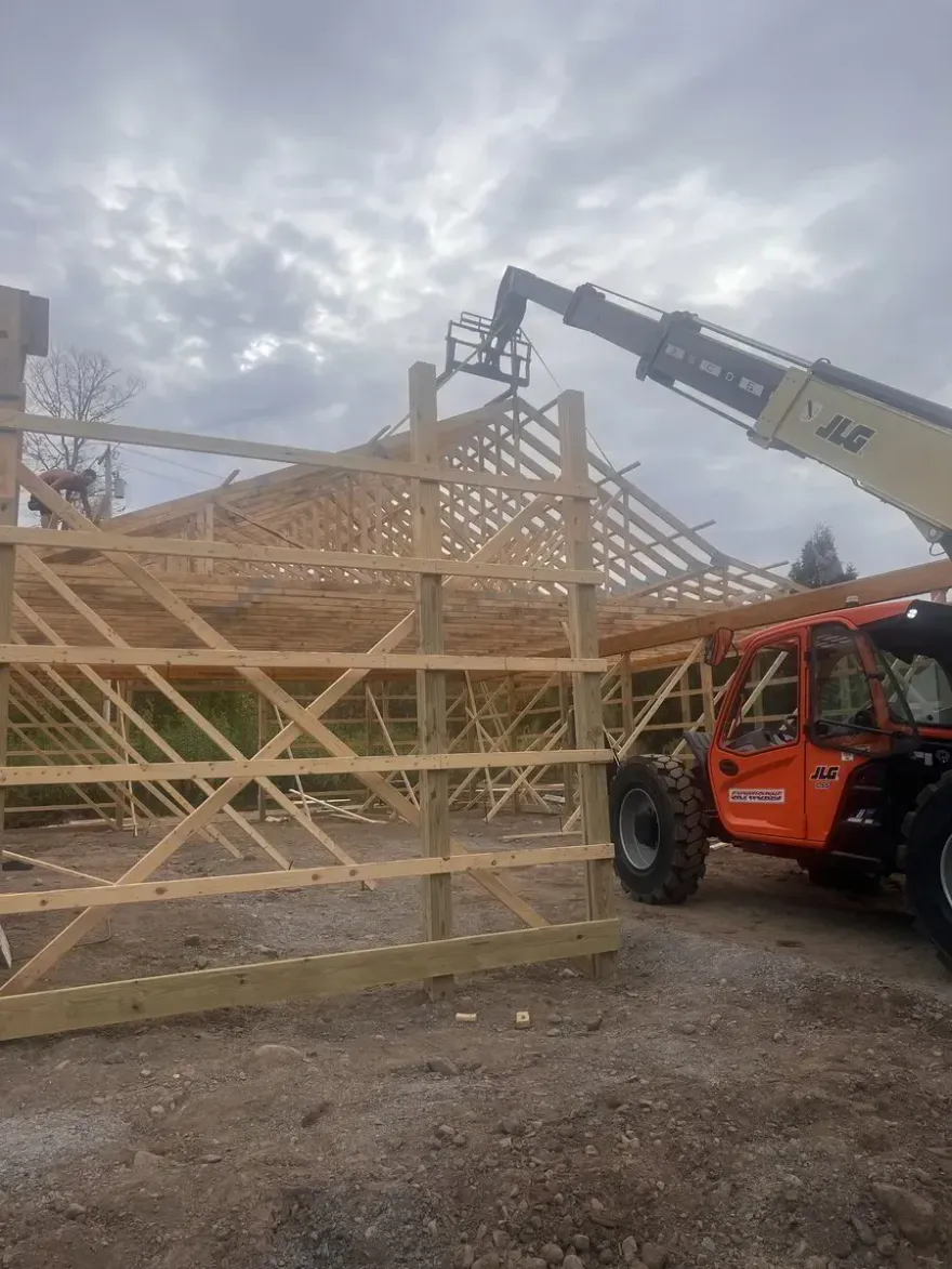 A construction worker in a raised telehandler platform works on the wooden roof trusses of a building under construction.