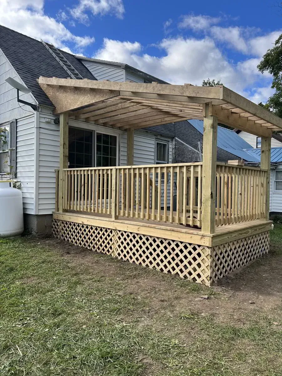 A newly constructed wooden deck with a slatted roof and lattice skirting attached to the back of a white house.