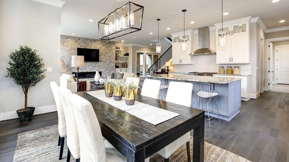 A spacious open-plan dining and kitchen area with dark wood floors, white dining chairs, and a grey kitchen island.
