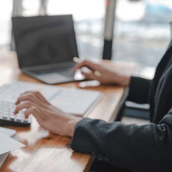 CPA in black blazer typing on laptop and calculator at a wooden desk.