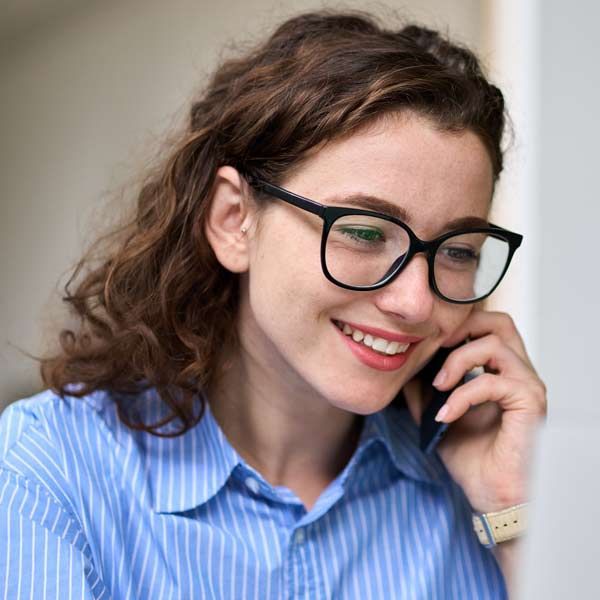 Woman wearing glasses smiles while talking on a phone, blue shirt Contact Solution Web Designs For A Free Consultation