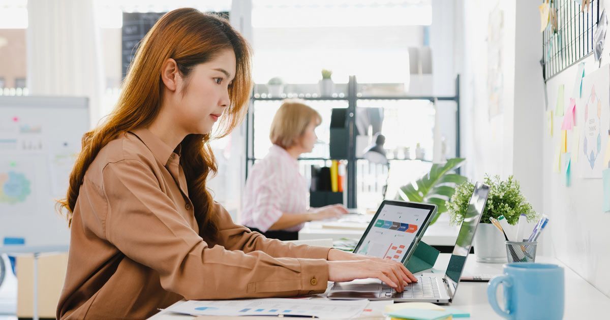 Website Copywriting Services by a Woman working on a laptop at a desk in an office setting.