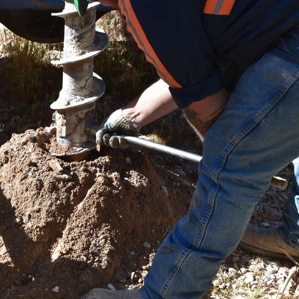 A Geotechnical Engineer using a powered auger to drill a hole in the earth.