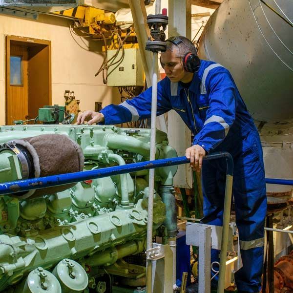 Marine Engineer in blue coveralls and ear protection, inspecting a large green engine.