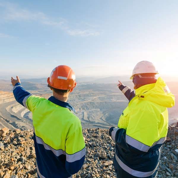 Mining Engineers in reflective vests and hard hats are pointing at a quarry.