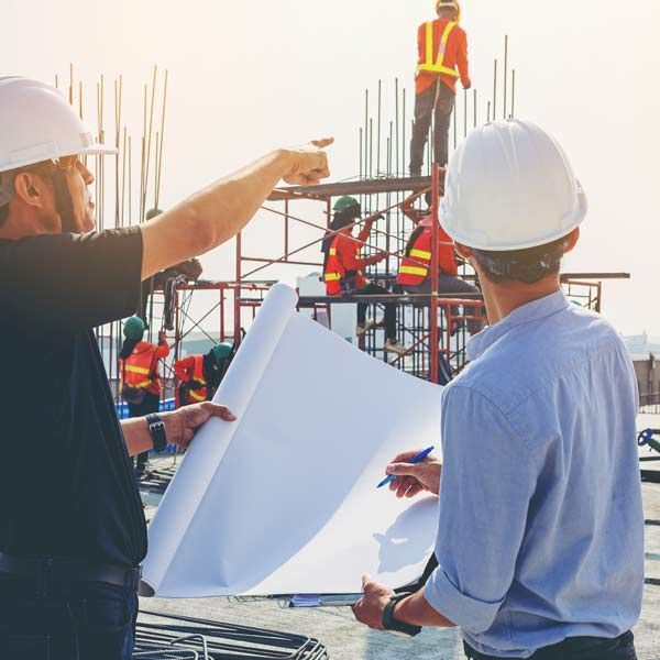 Two Structural Engineers review blueprints on a building site, pointing and consulting.
