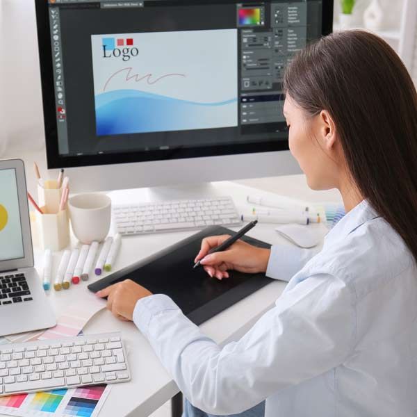 A female graphic artist using a digital pen on a tablet to design a logo on a computer monitor.