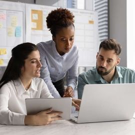 A team of online marketers collaborating around a laptop and tablet in an office setting.