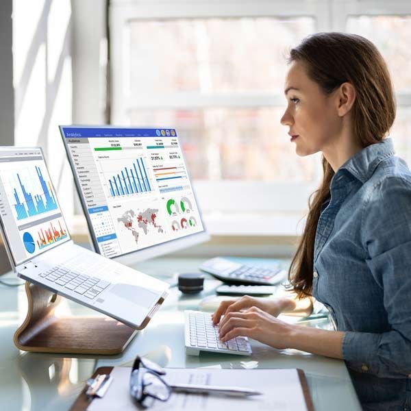 Woman working on a computer with multiple Performance Analytics and Conversion ROI Tracking data visualizations displayed on screens in an office setting.