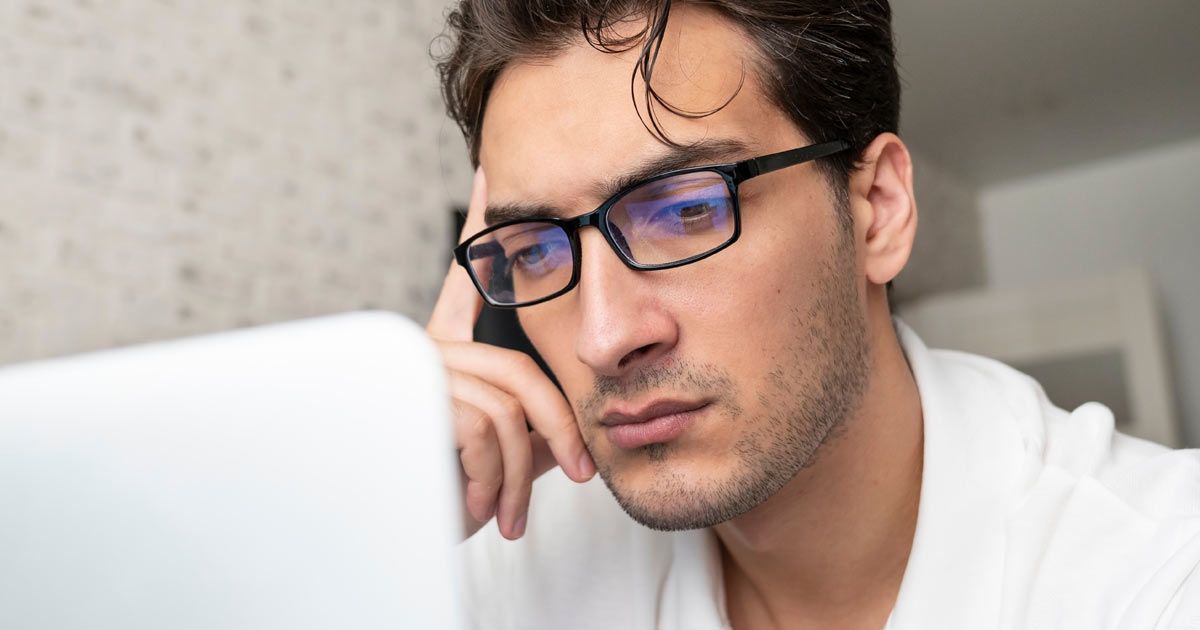 Man with glasses looking intently at a laptop, hand on forehead realizing he needs Online Reputation Management Services - Solution Web Designs