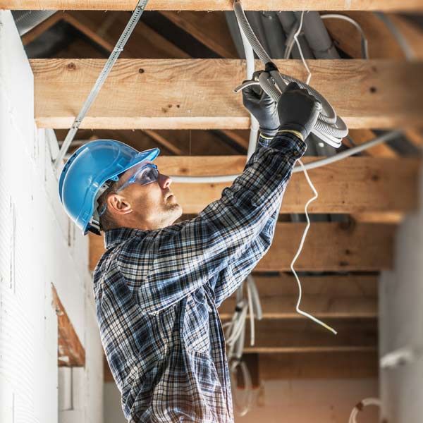 Electrician in a hard hat working on wiring inside a building.