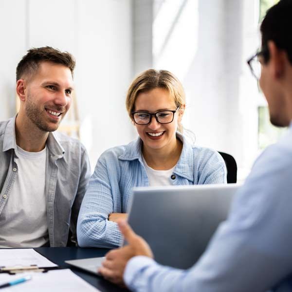 Couple smiling at a Financial Advisor a laptop screen, likely a consultation in an office setting.