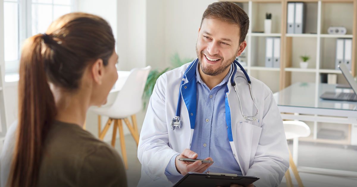 Doctor smiling at patient in a medical office, holding a clipboard after patient searched Websites for Functional Medicine Doctors