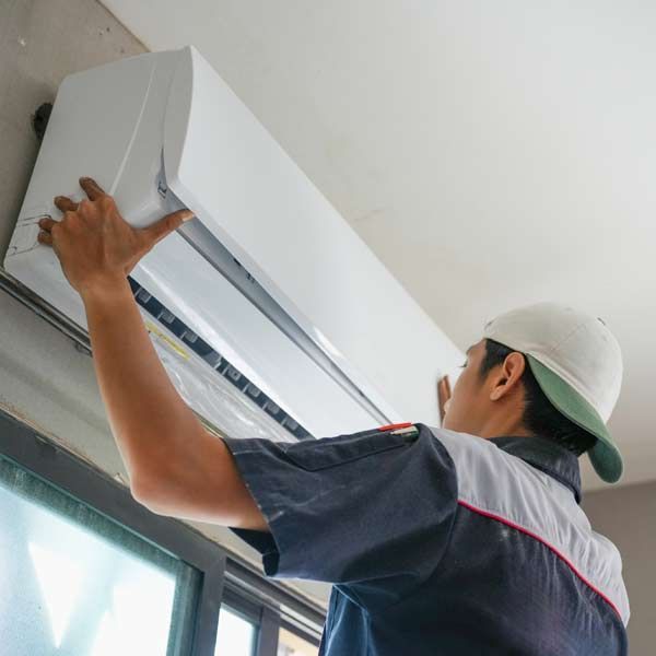HVAC Technician in work uniform installing a white air conditioner on a wall.