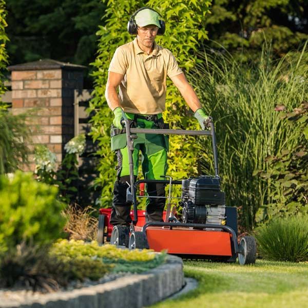Landscaping and lawn care man mowing the lawn with a red machine, wearing hearing protection, in a sunny garden.