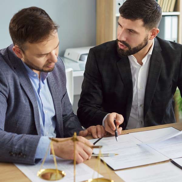 A lawyer and his client are reviewing documents at a table; scales of justice in the foreground.