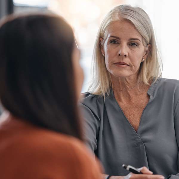 A Mental Health Provider female with gray hair intently listens to another person in an office setting.