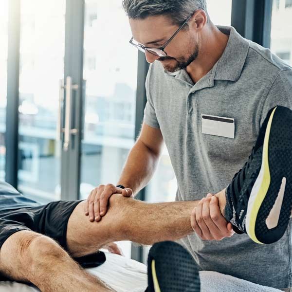 A physical therapist examining a patient's knee in an office, indoors, holding the patient’s leg.