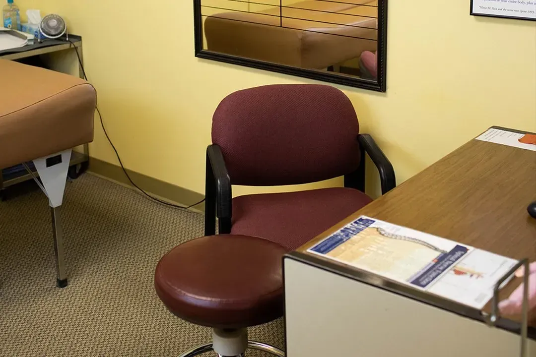 Empty office chair beside desk in a small beige office with a wall mirror and filing items