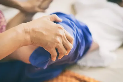 Hands gently holding a baby wrapped in a blue blanket on a soft bed