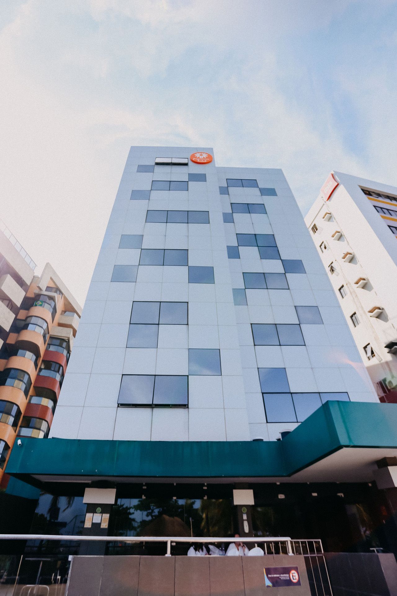 Prédio alto e moderno com detalhes em turquesa e fachada quadriculada. Céu nublado.