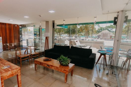 Hall de entrada moderno com sofá preto, móveis de madeira e janelas de vidro com vista para a praia.