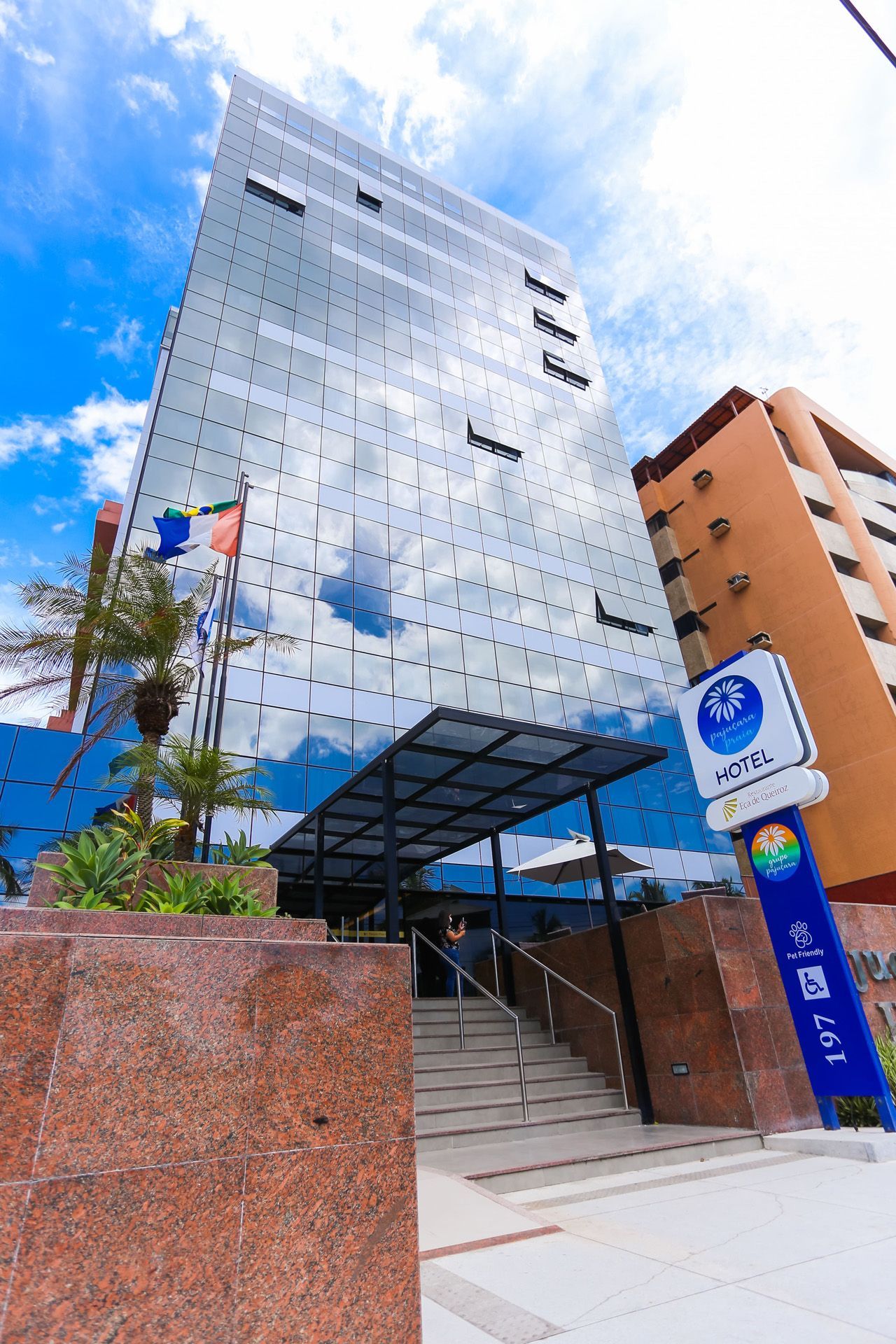 Prédio moderno de vidro com reflexo do céu azul; uma placa com o nome 