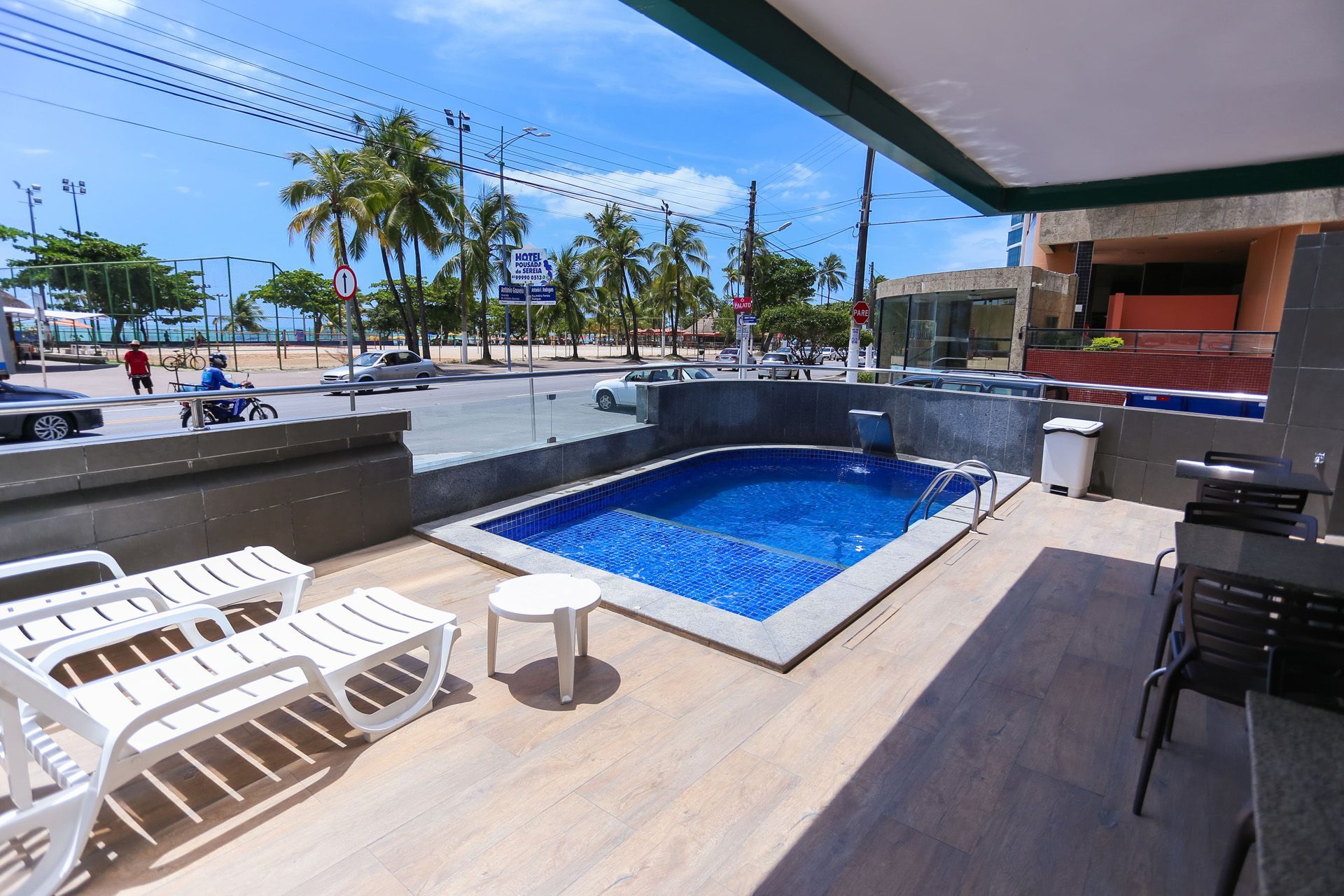 Área da piscina com uma pequena piscina, espreguiçadeiras e vista para a praia e para a rua.