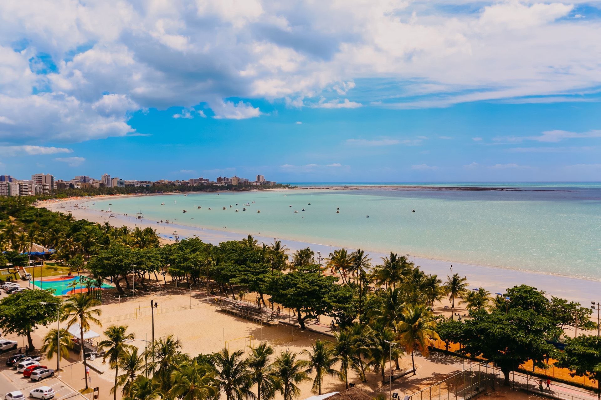 Grande edifício azul e branco, provavelmente um hospital ou escritório, cercado por estradas, árvores e carros estacionados.