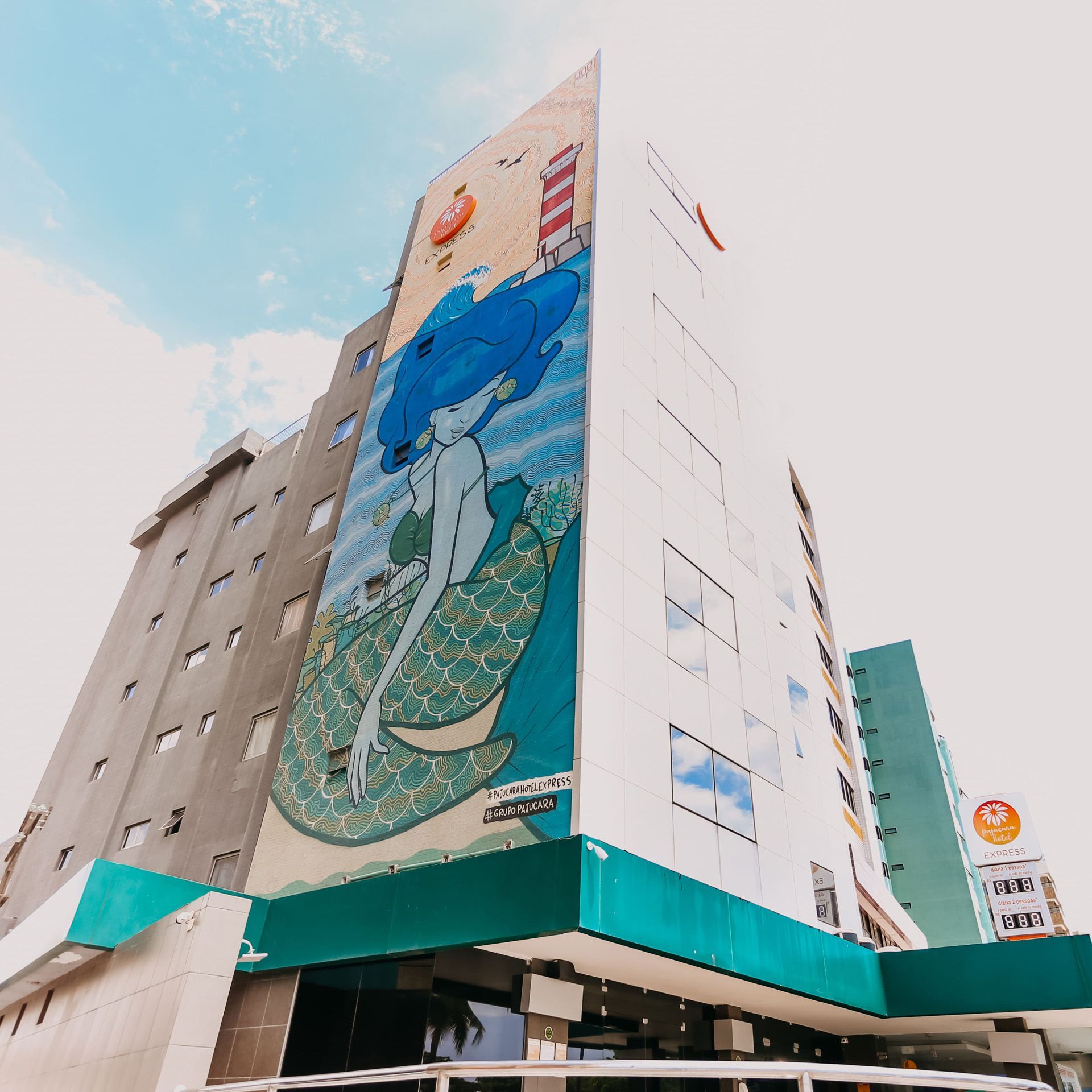 Hotel moderno com fachada amarela e cinza, rua com trânsito e horizonte da cidade.