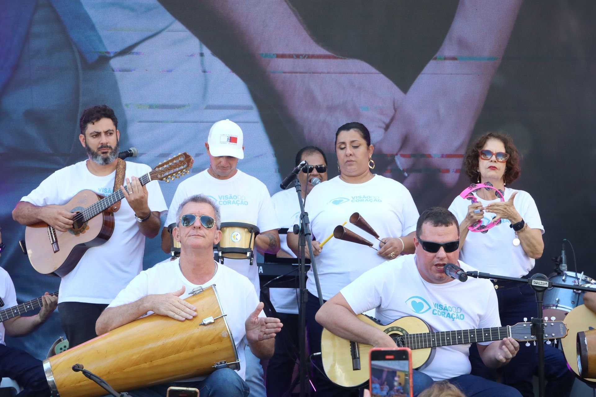 A group of people are playing instruments in front of a large screen.
