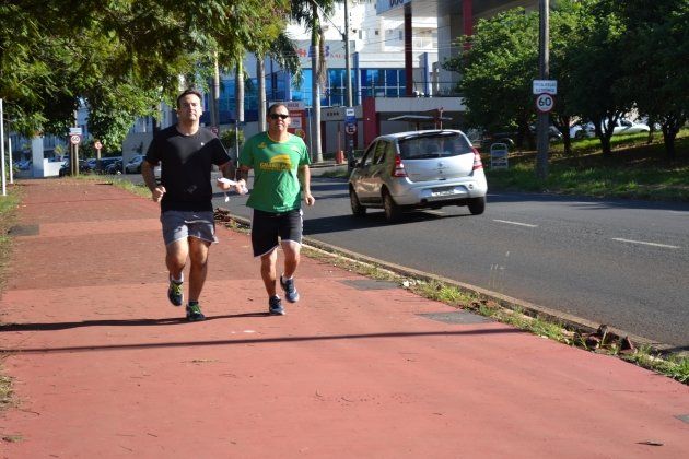 Dois homens estão correndo em uma calçada ao lado de uma estrada.