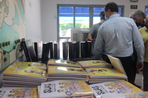 Um grupo de pessoas está em pé ao redor de uma mesa com livros sobre ela que dizem suas