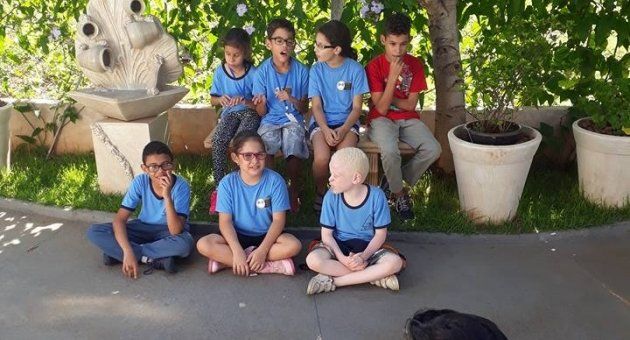 Um grupo de crianças está sentado no chão em frente a uma fonte.