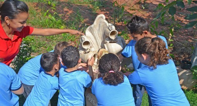 Um grupo de crianças de camisa azul olha para uma estátua.