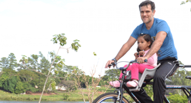 Um homem está andando de bicicleta com uma menina na cadeirinha.