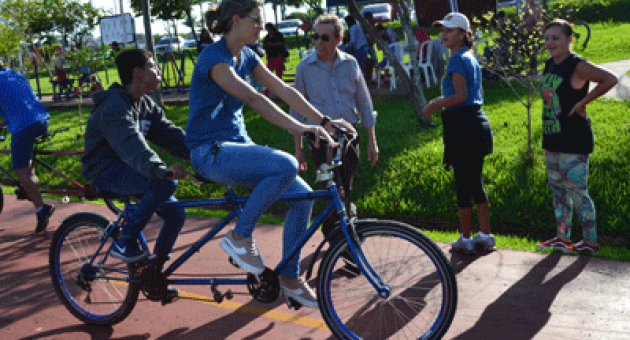 Uma mulher está andando de bicicleta dupla com uma criança nas costas.