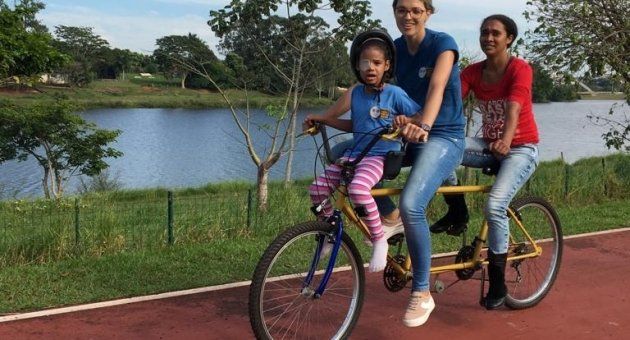 Duas mulheres e uma criança estão andando de bicicleta dupla.