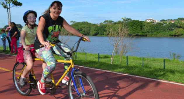 Uma mulher está andando de bicicleta dupla com uma criança nas costas.