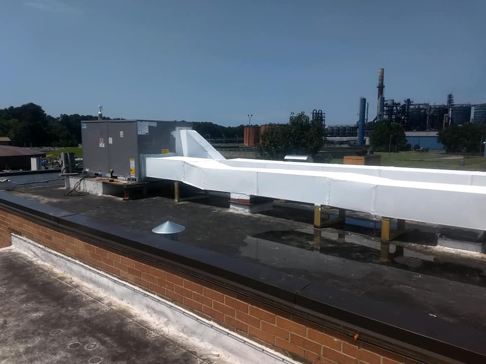 Rooftop with white ductwork, vents, and industrial backdrop under a blue sky.