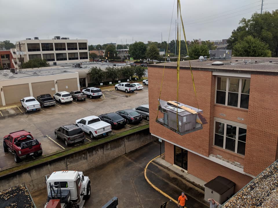 Hands wearing red and black gloves using a screwdriver on a white appliance.