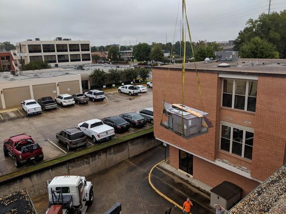 Hands wearing red and black gloves using a screwdriver on a white appliance.