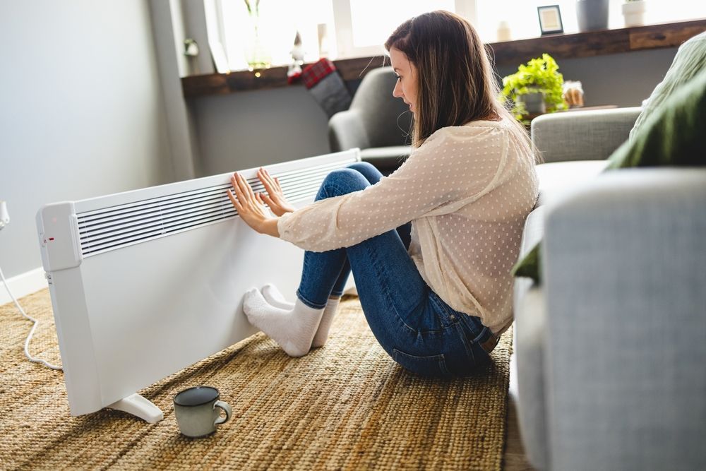 A woman is sitting on the floor in front of a heater.