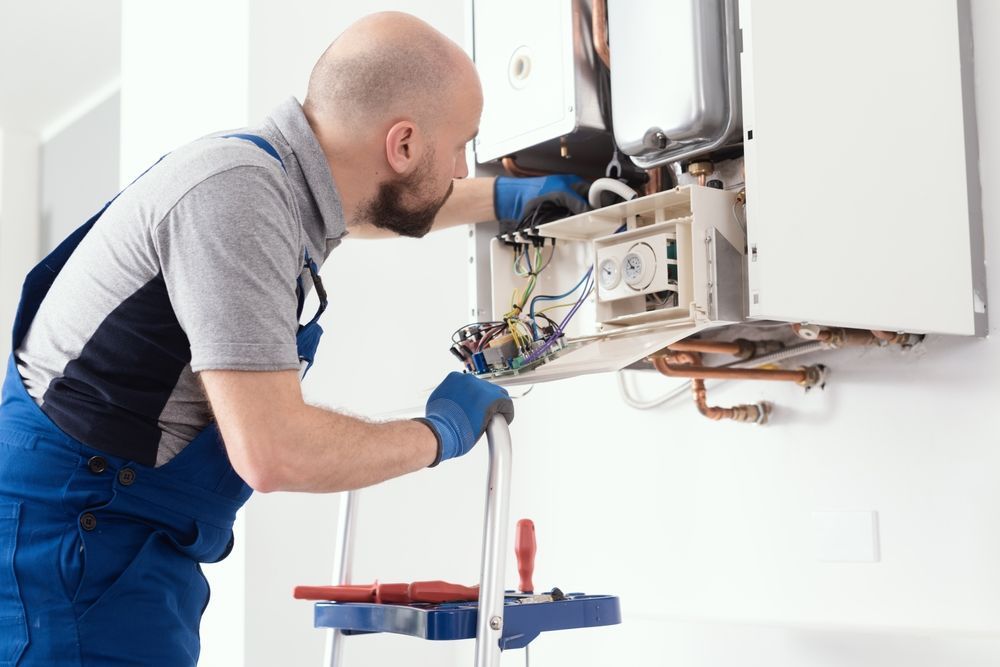 A man is working on a boiler on a ladder.