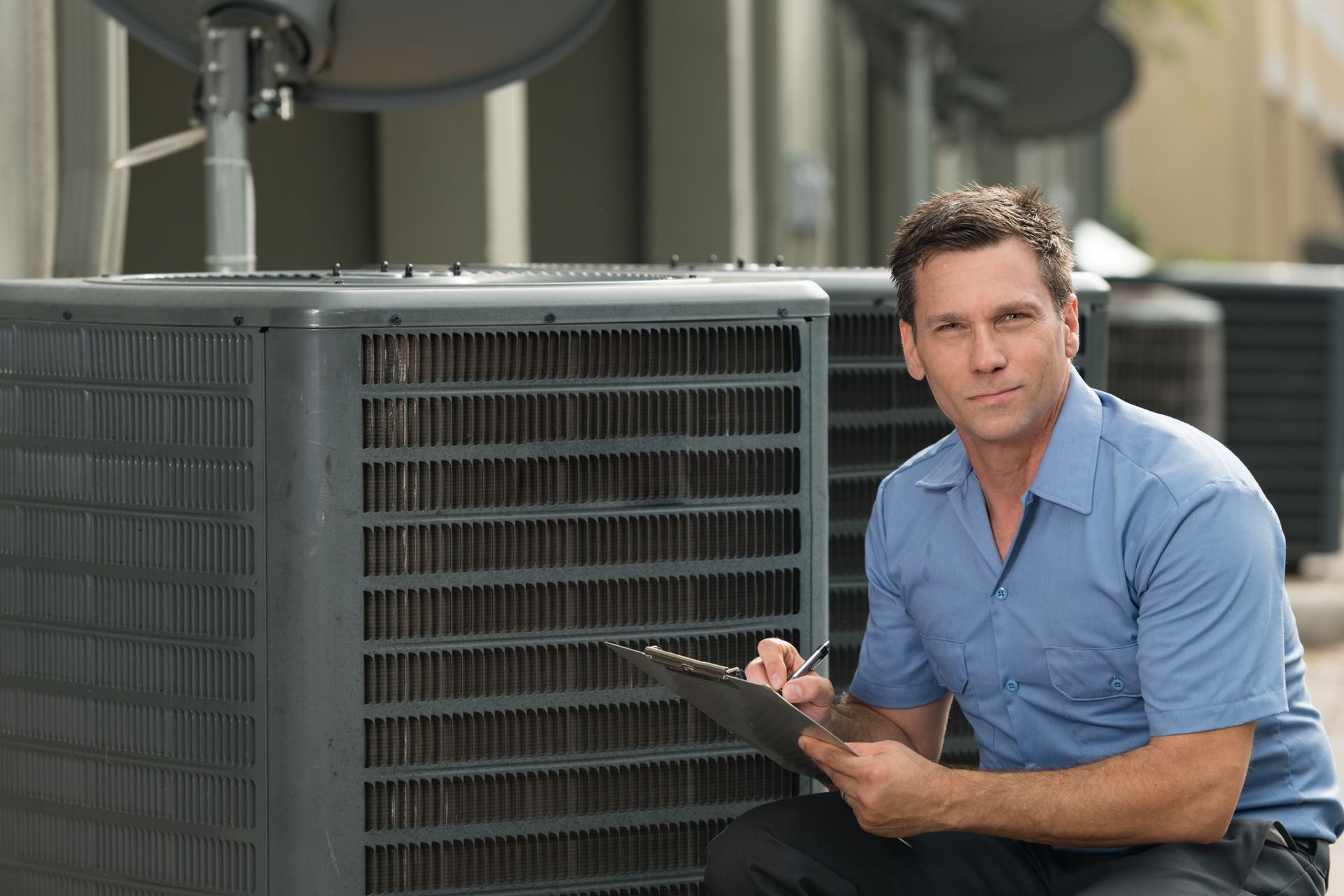 HVAC technician kneeling by outdoor AC unit, taking notes on clipboard.